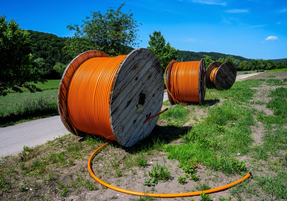 Déploiement de la fibre optique : bobines de câble orange Trois grandes bobines de câble orange sur le bord d'une route pour le déploiement de la fibre optique en campagne.