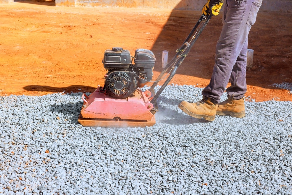Compactage du gravier avec une plaque vibrante sur chantier Ouvrier utilisant une plaque vibrante pour compacter du gravier sur un chantier de construction.