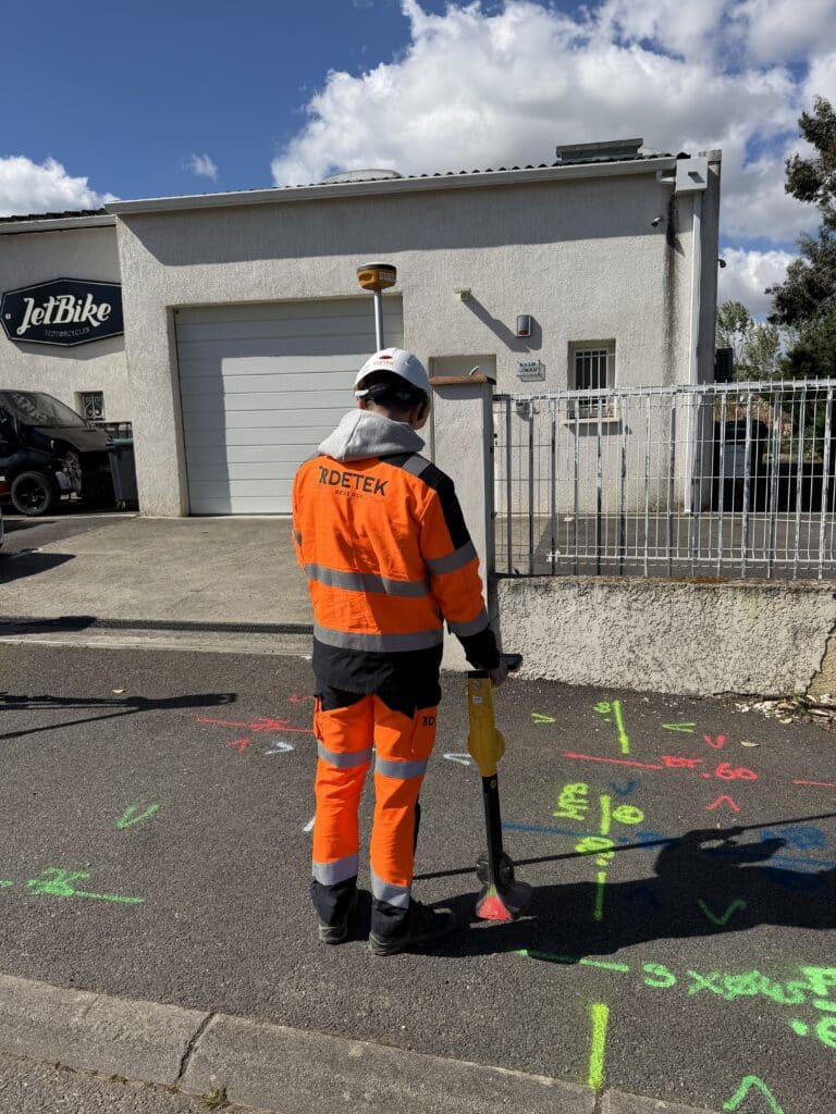 Détection de réseaux enterrés et marquages par RDETEK Technicien RDETEK utilisant un localisateur sur marquages au sol colorés devant le garage JetBike.