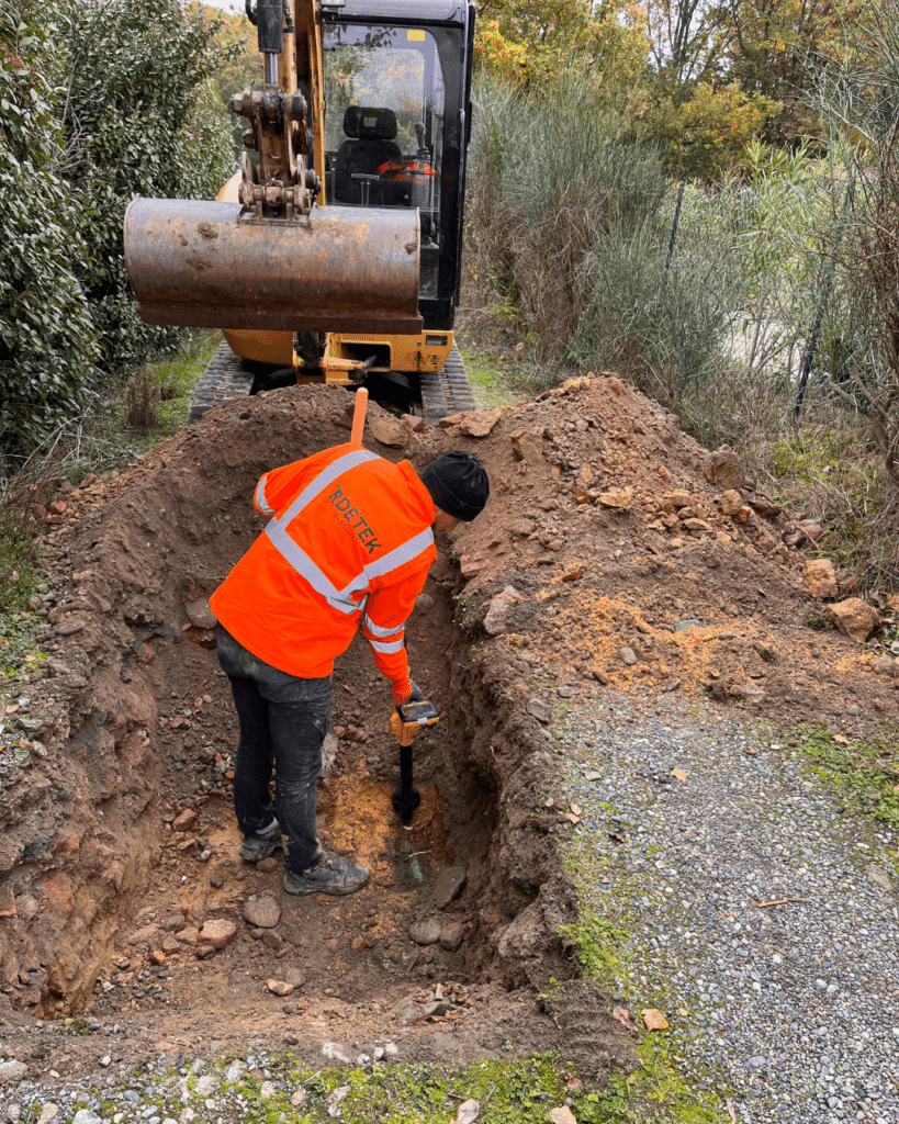 Détection de réseaux IRDETEK : Excavation et Travaux Technicien IRDETEK RÉSEAUX utilisant un détecteur de câbles dans une tranchée avec une mini-pelleteuse.
