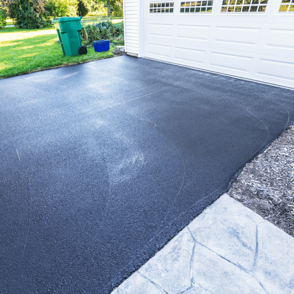 Asphalte scellé : protection durable pour allée de garage Allée de garage en asphalte avec scellant protecteur noir devant une porte blanche, offrant un aspect neuf et durable.