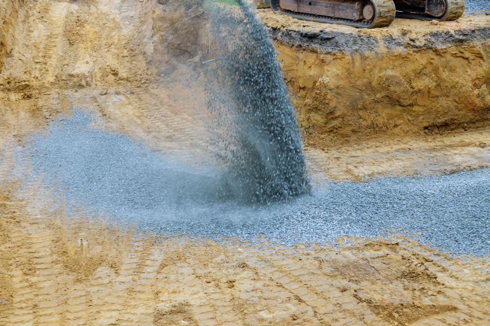 Gravier de construction pour remblayage et terrassement Gravier bleu déversé dans une excavation sur un chantier de construction avec chenilles d'engin visibles.