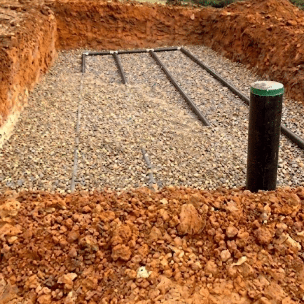 Installation de drainage : pose de tuyaux sur lit de gravier Installation d'un système de drainage avec tuyaux perforés sur lit de gravier dans une excavation en terre rouge.