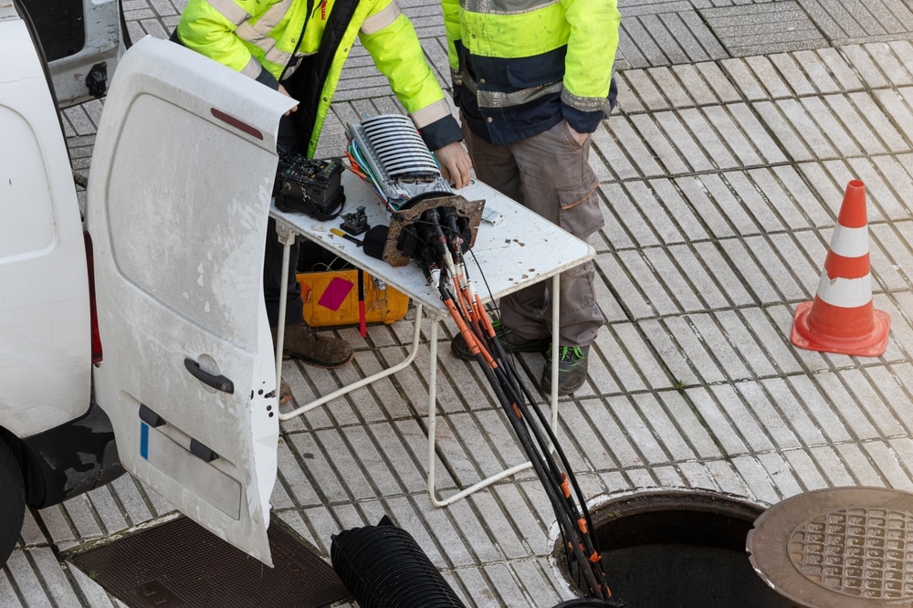 Installation et maintenance de fibre optique en extérieur Techniciens installant la fibre optique sur un trottoir avec une épissure et des câbles sortant d'un regard.