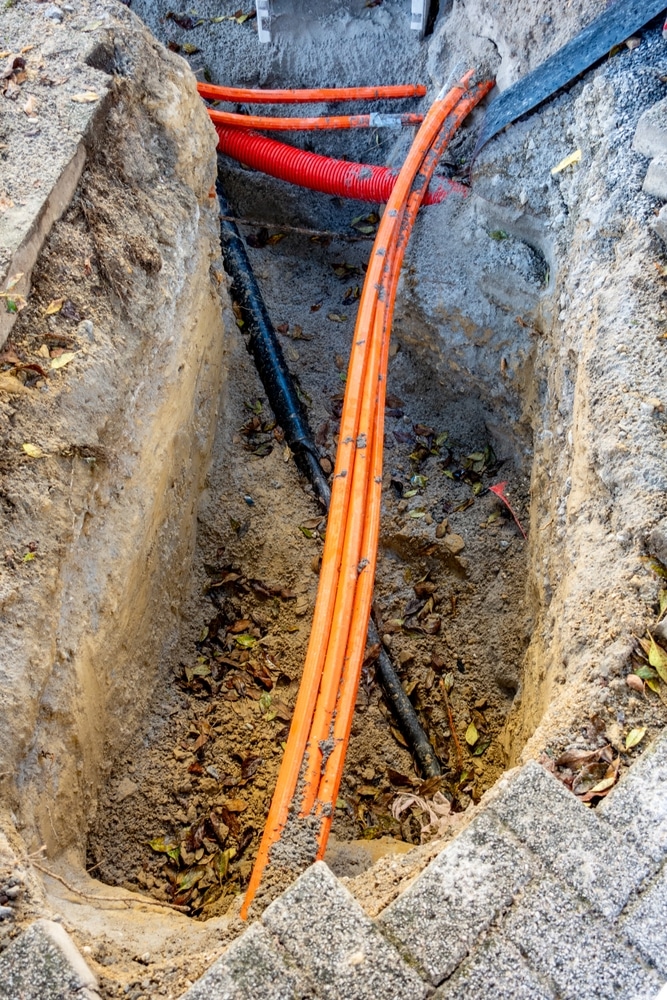 Déploiement de la fibre optique en tranchée urbaine Câbles de fibre optique orange et conduits dans une tranchée de chantier lors de travaux de voirie urbains.