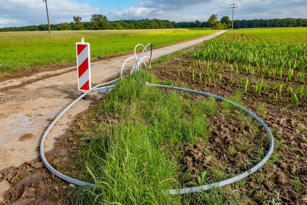 Fibre optique : installation de câbles en zone rurale Câble de fibre optique gris en boucle sur un chemin rural près d'une balise de signalisation rouge et blanche.