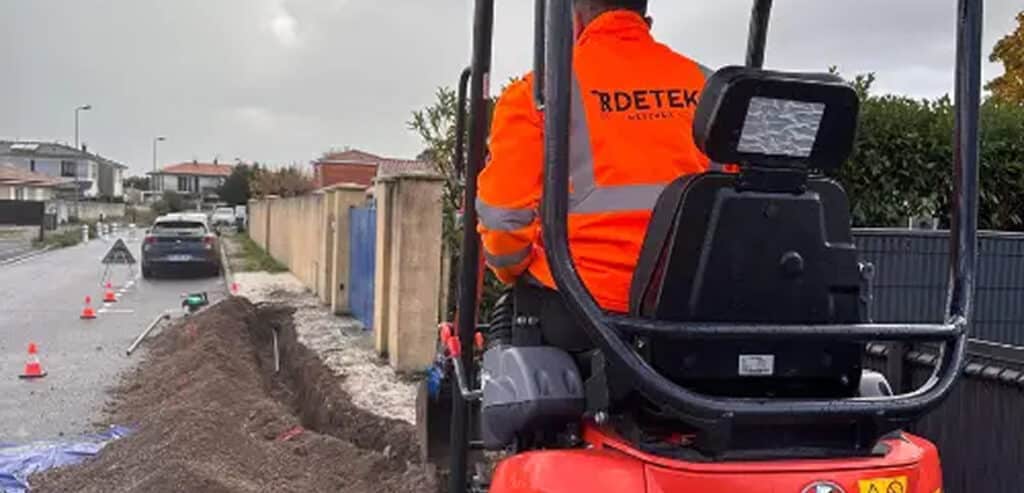 Mini pelle RDETEK pour travaux de terrassement urbain Opérateur RDETEK pilotant une mini pelle pour creuser une tranchée de terrassement le long d'une rue résidentielle.