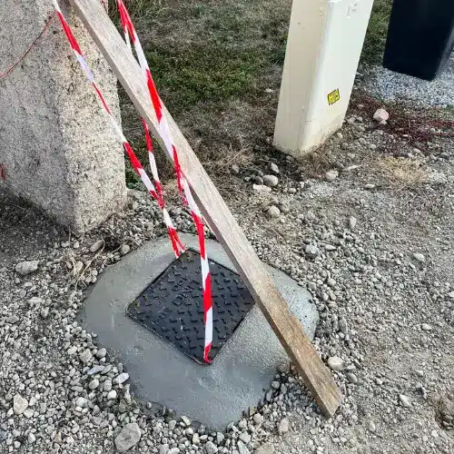 Installation d'un regard de chaussée LIND A125 en béton Regard LIND A125 scellé dans du béton frais avec ruban de signalisation et planche de protection sur chantier.