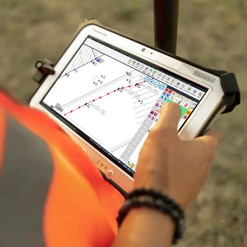 Tablette Panasonic Toughpad pour Relevé Topographique Géomètre utilisant une tablette Panasonic Toughpad affichant un plan de relevé topographique 101.00 sur le terrain.