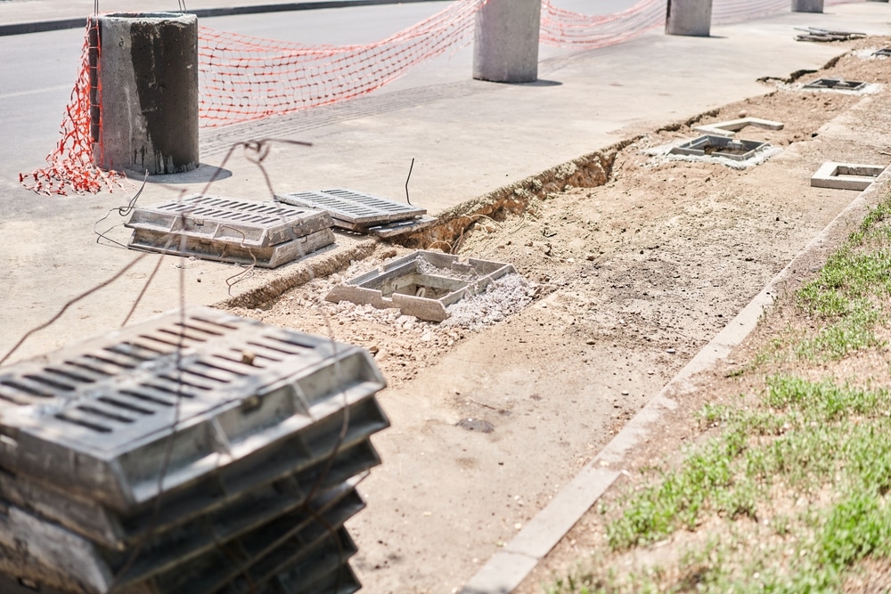 Travaux de drainage : installation de grilles d'égouts Chantier de voirie : grilles d'égouts empilées, cadres en béton et tranchée de drainage le long du trottoir.