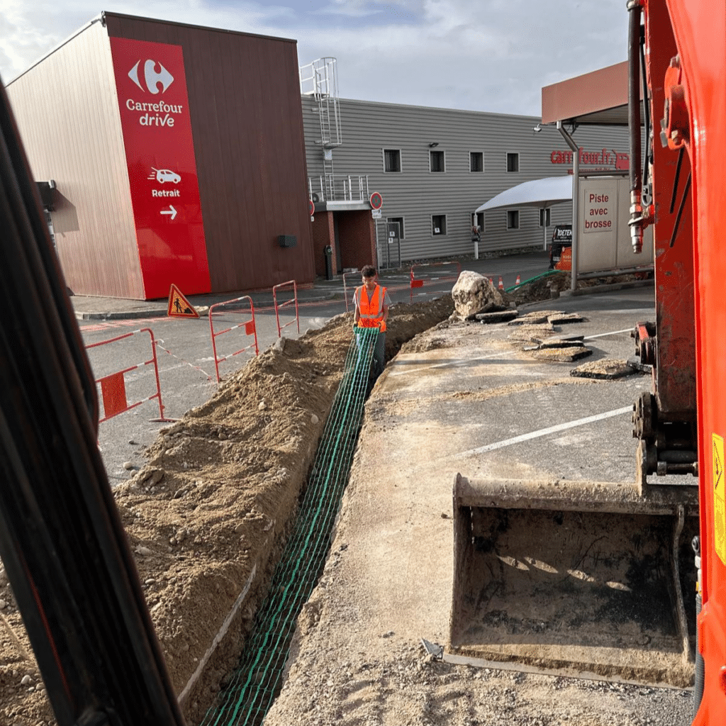 Travaux de terrassement Carrefour Drive : pose de réseau Ouvrier posant un grillage avertisseur vert dans une tranchée Carrefour Drive, travaux de terrassement et réseaux.