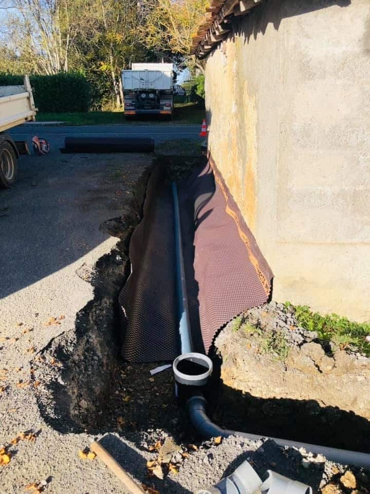 Installation de drainage et étanchéité des fondations Installation d'un drainage périphérique avec membrane alvéolée et tuyau PVC le long d'un mur de fondation en chantier.