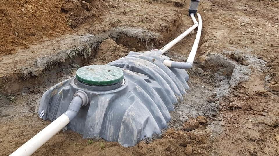 Fosse septique en plastique gris avec couvercle vert et raccordements PVC dans une tranchée d'assainissement.